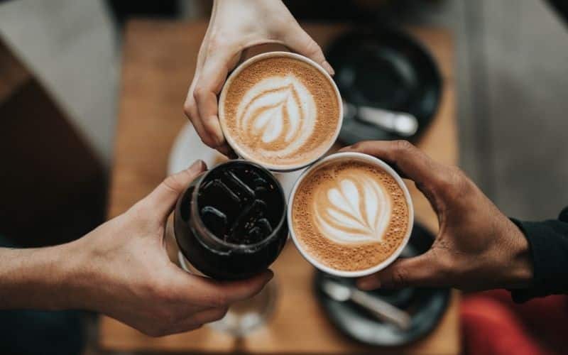 Three hands toasting with coffee, two lates and one cold brew